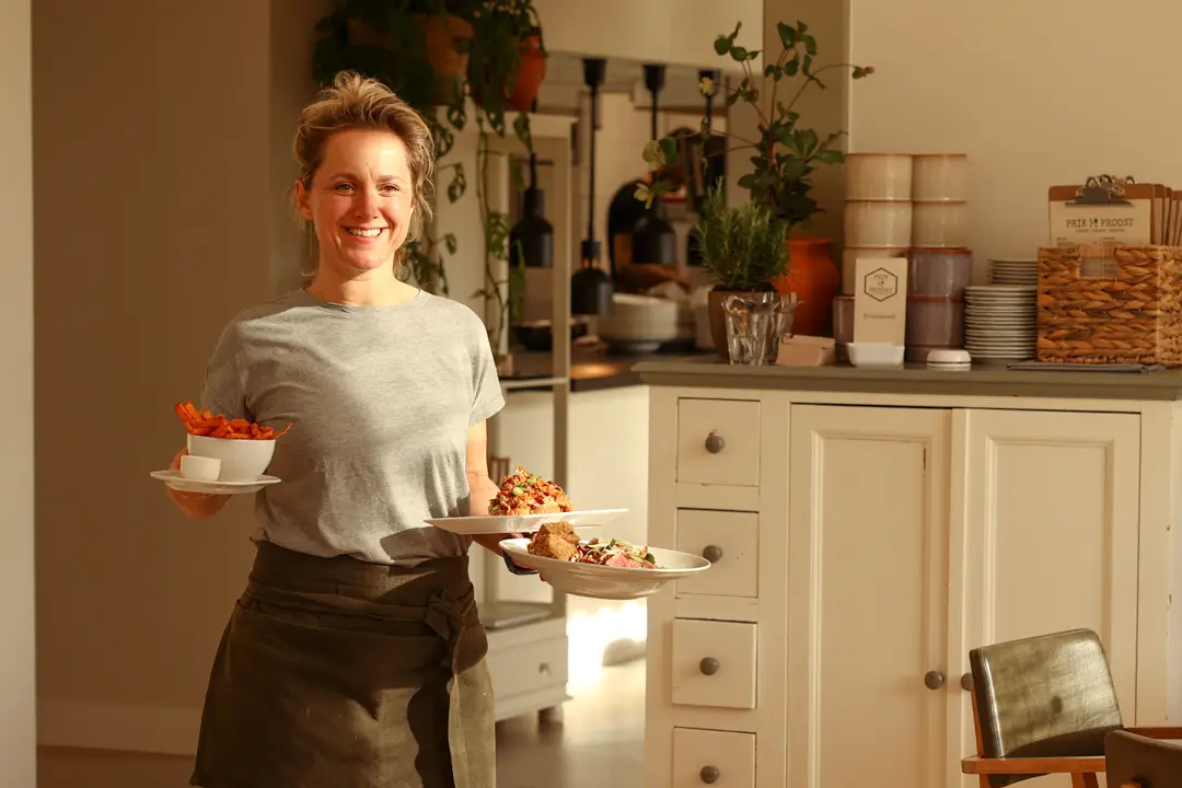 Glimlachende medewerker loopt met drie borden eten door het restaurant