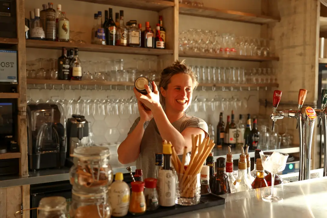 Barmedewerker schudt lachend een cocktail achter de bar