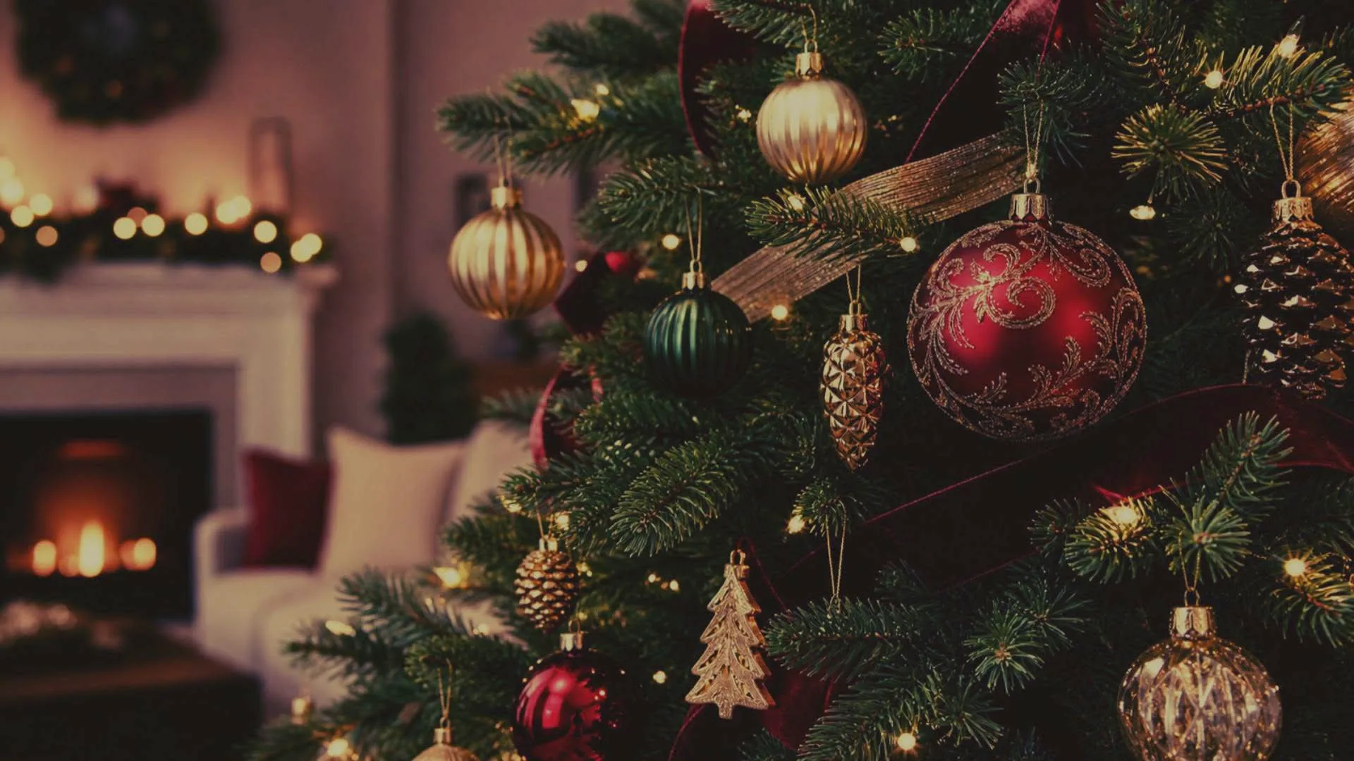 Kerstboom met rode, gouden en groene kerstballen en lichtjes, met op de achtergrond een open haard