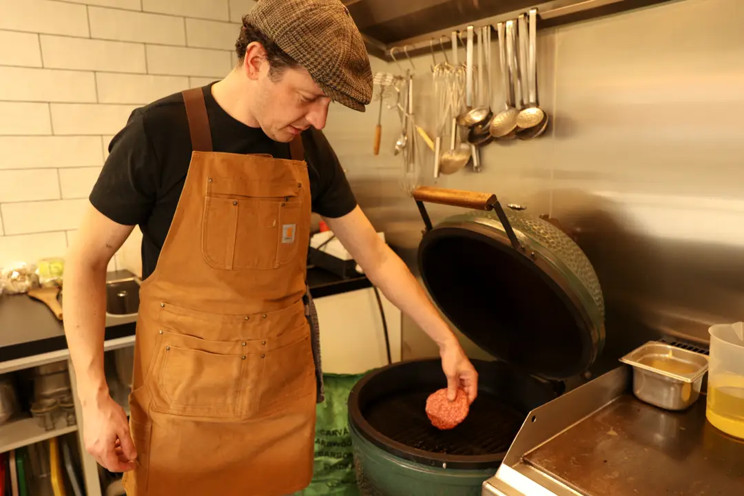 Kok legt een hamburger op de grill in de open keuken