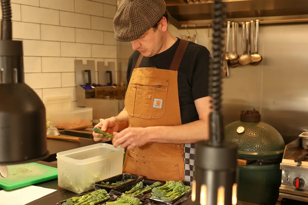 Kok maakt broccolini schoon in de open keuken, met warmhoudlampen op de voorgrond