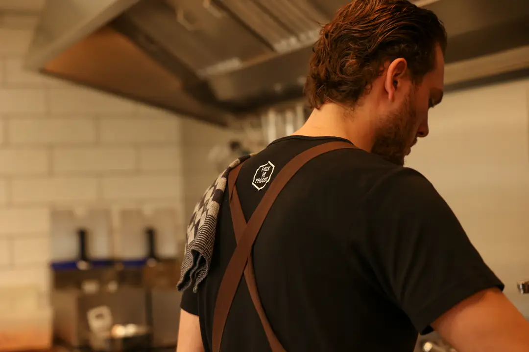 Kok in zwart shirt met het Prik & Proost-logo aan het werk in de keuken