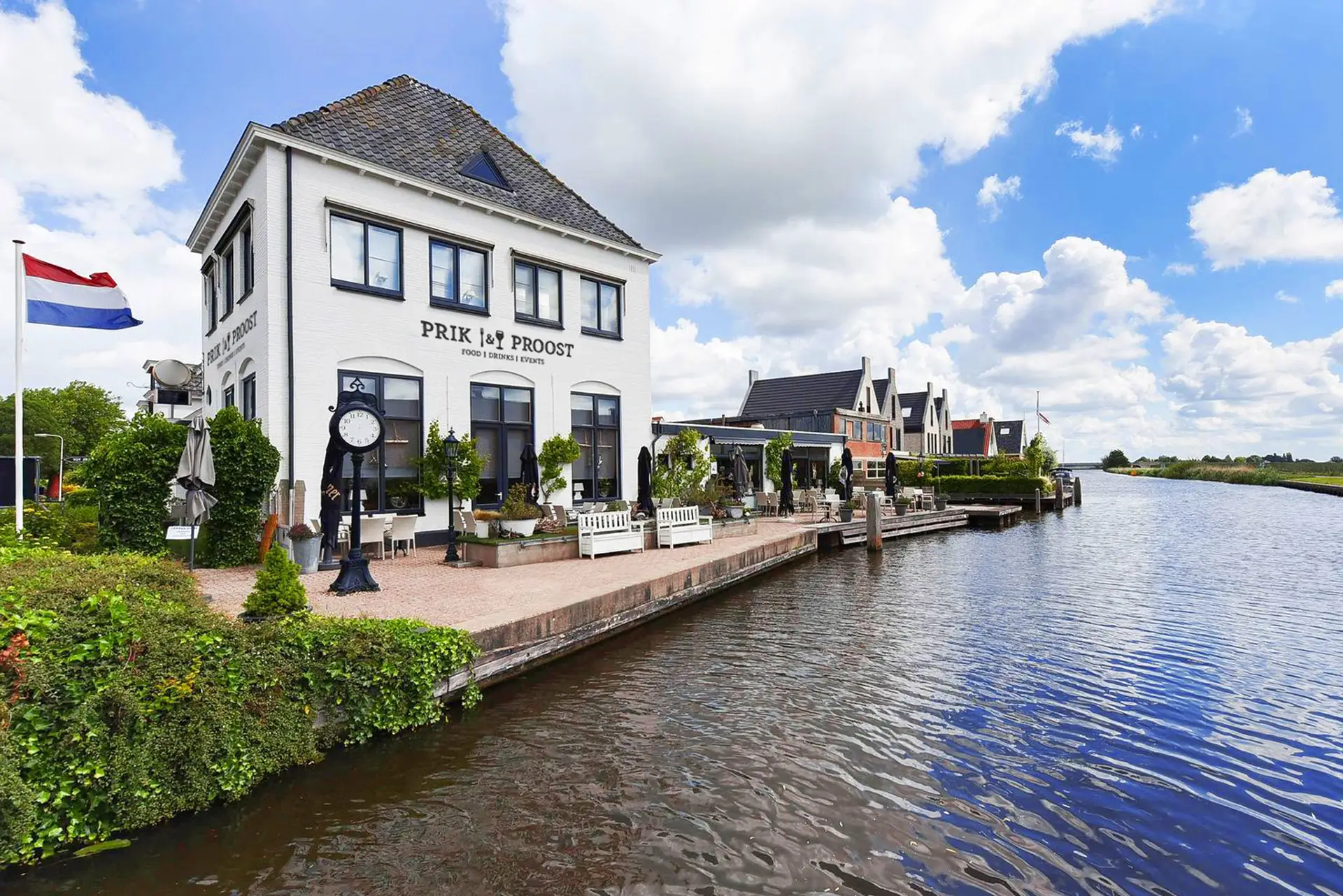 Wit pand van Prik & Proost aan de Drecht, met terras aan het water en de Nederlandse vlag