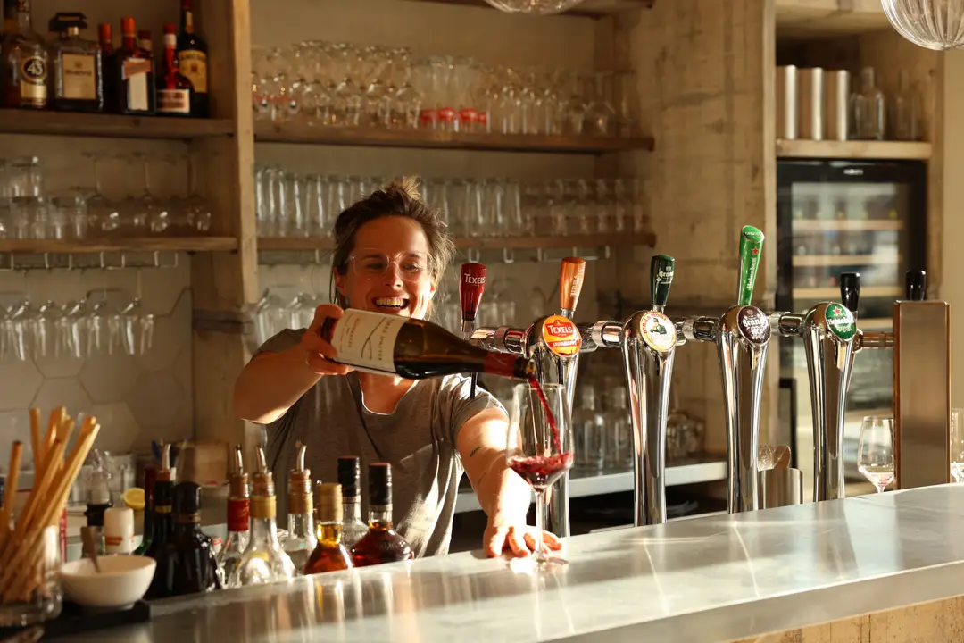 Barmedewerker schenkt lachend een glas rode wijn in aan de bar