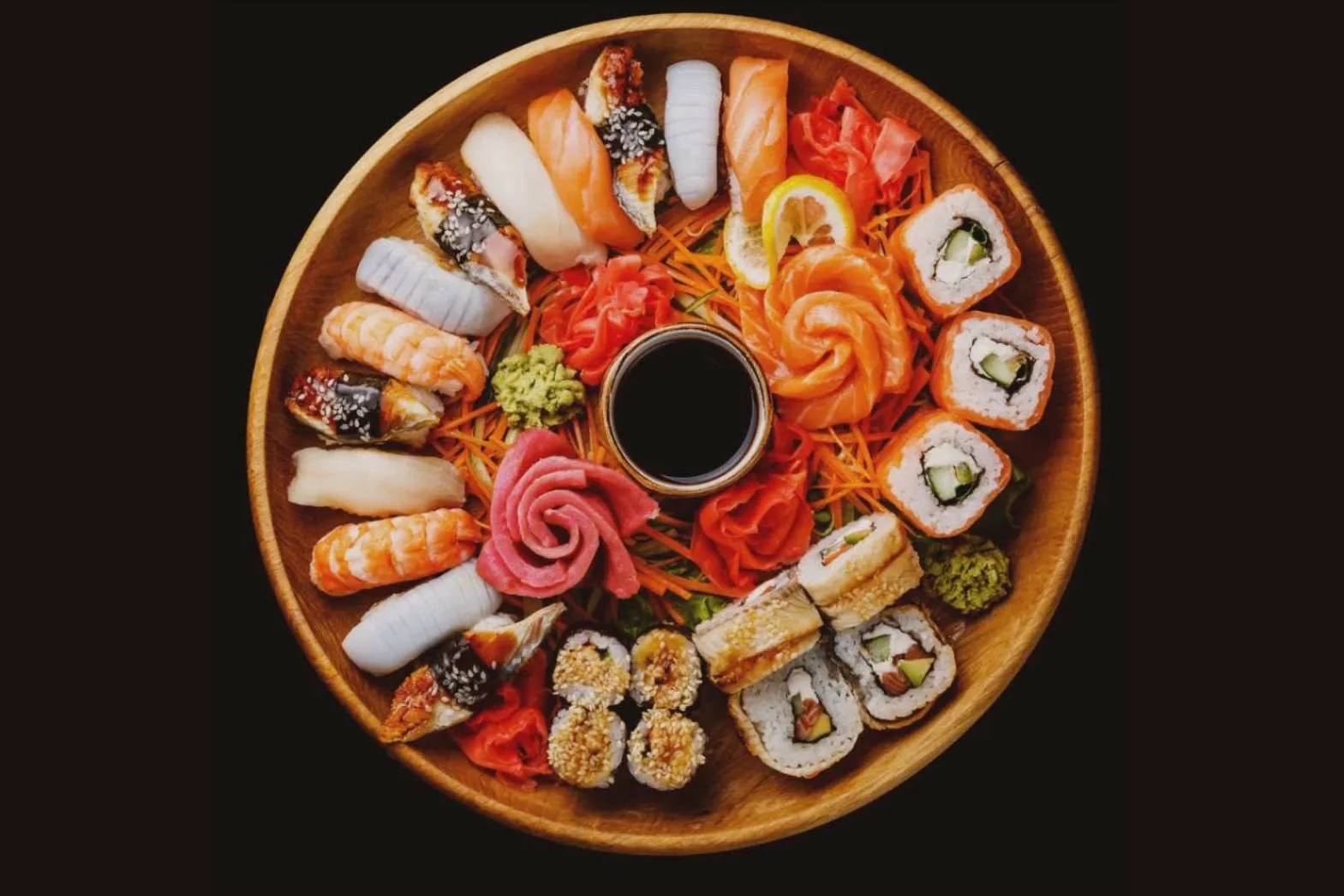 Bovenaanzicht van een houten schaal met sushi, sashimi, gember en wasabi rond een schaaltje sojasaus